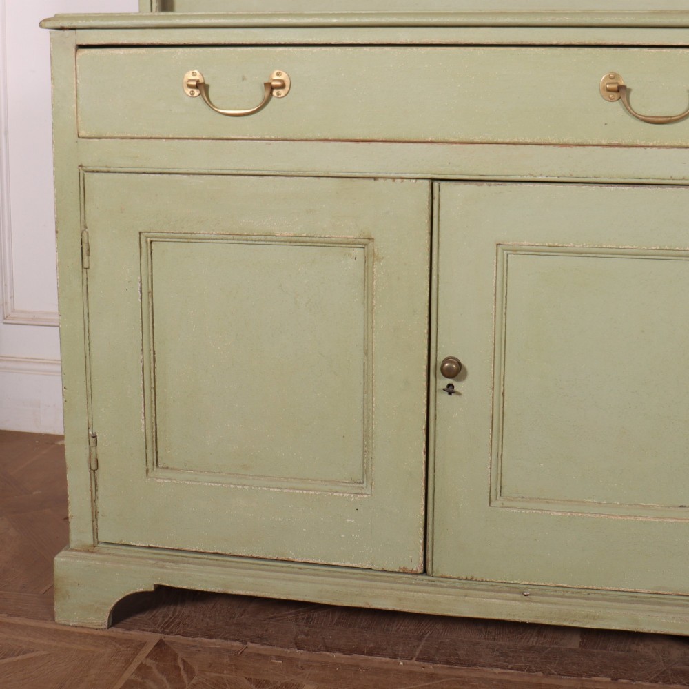 A large sage green painted dresser featuring an upper glazed display cabinet with sliding doors, lower drawers with brass drop handles, and panelled cupboard doors. View V