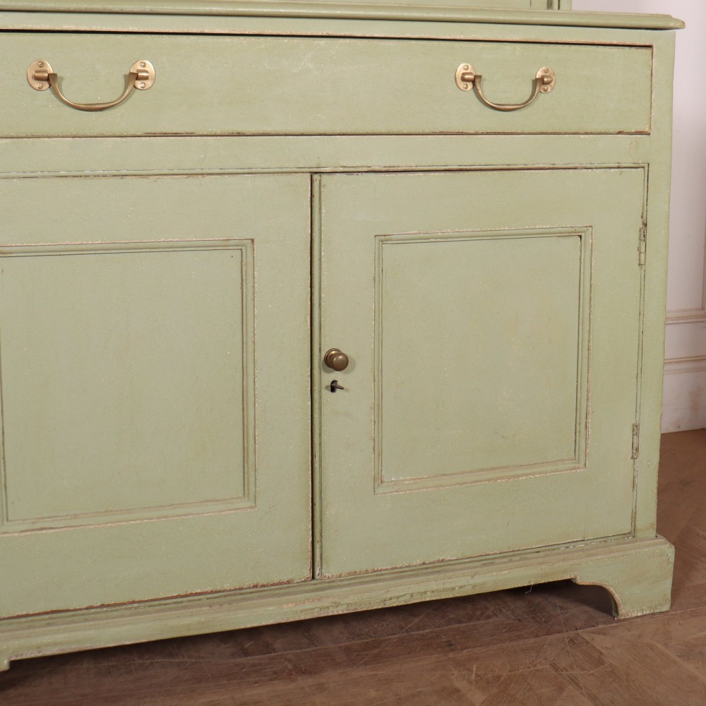 A large sage green painted dresser featuring an upper glazed display cabinet with sliding doors, lower drawers with brass drop handles, and panelled cupboard doors. View VI