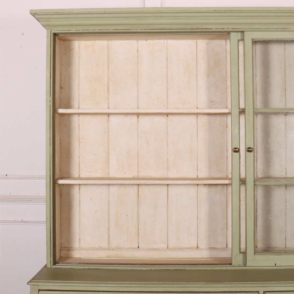 A large sage green painted dresser featuring an upper glazed display cabinet with sliding doors, lower drawers with brass drop handles, and panelled cupboard doors. View IX