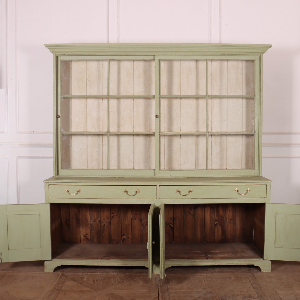 A large sage green painted dresser featuring an upper glazed display cabinet with sliding doors, lower drawers with brass drop handles, and panelled cupboard doors. View XI
