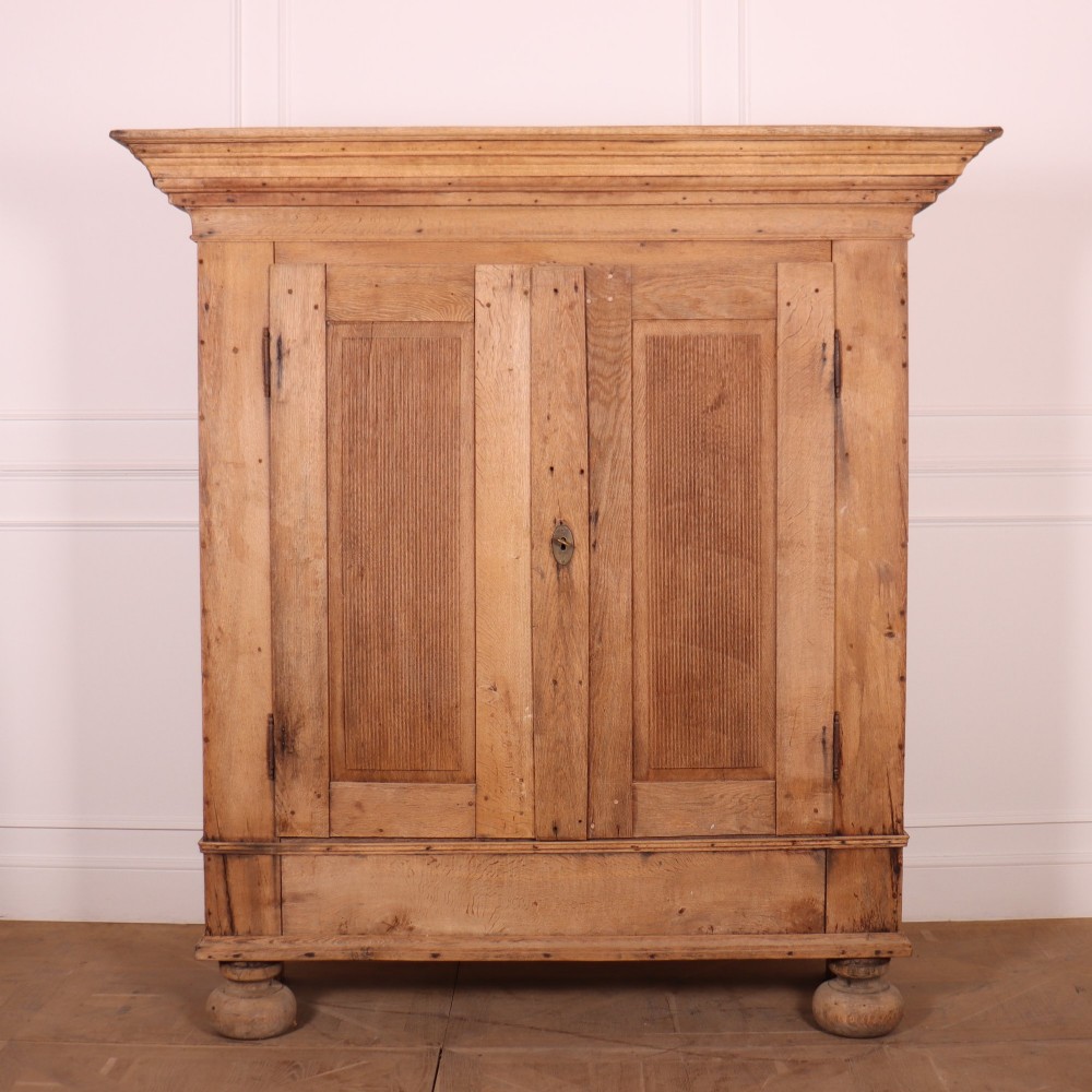 A freestanding antique Danish oak wardrobe featuring a flared top cornice, double doors with reeded panels, and heavy turned bun feet.