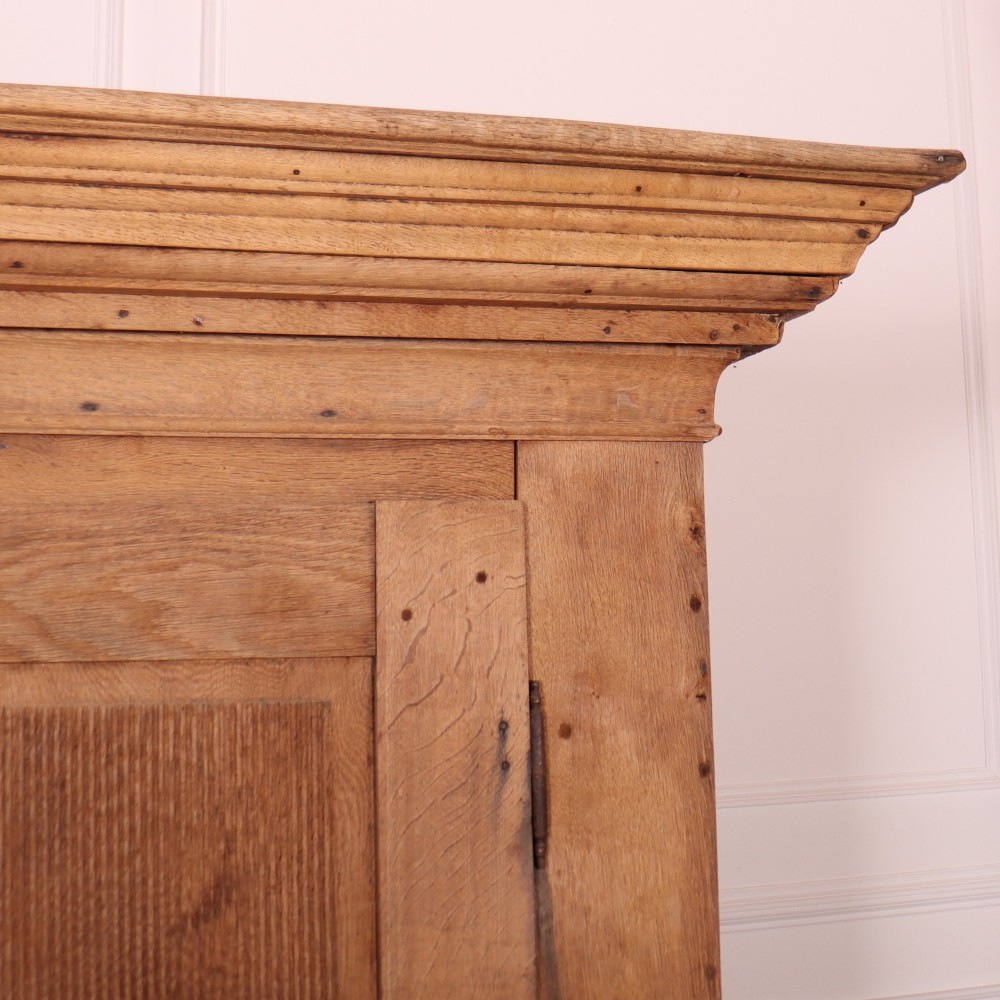 A freestanding antique Danish oak wardrobe featuring a flared top cornice, double doors with reeded panels, and heavy turned bun feet. View III