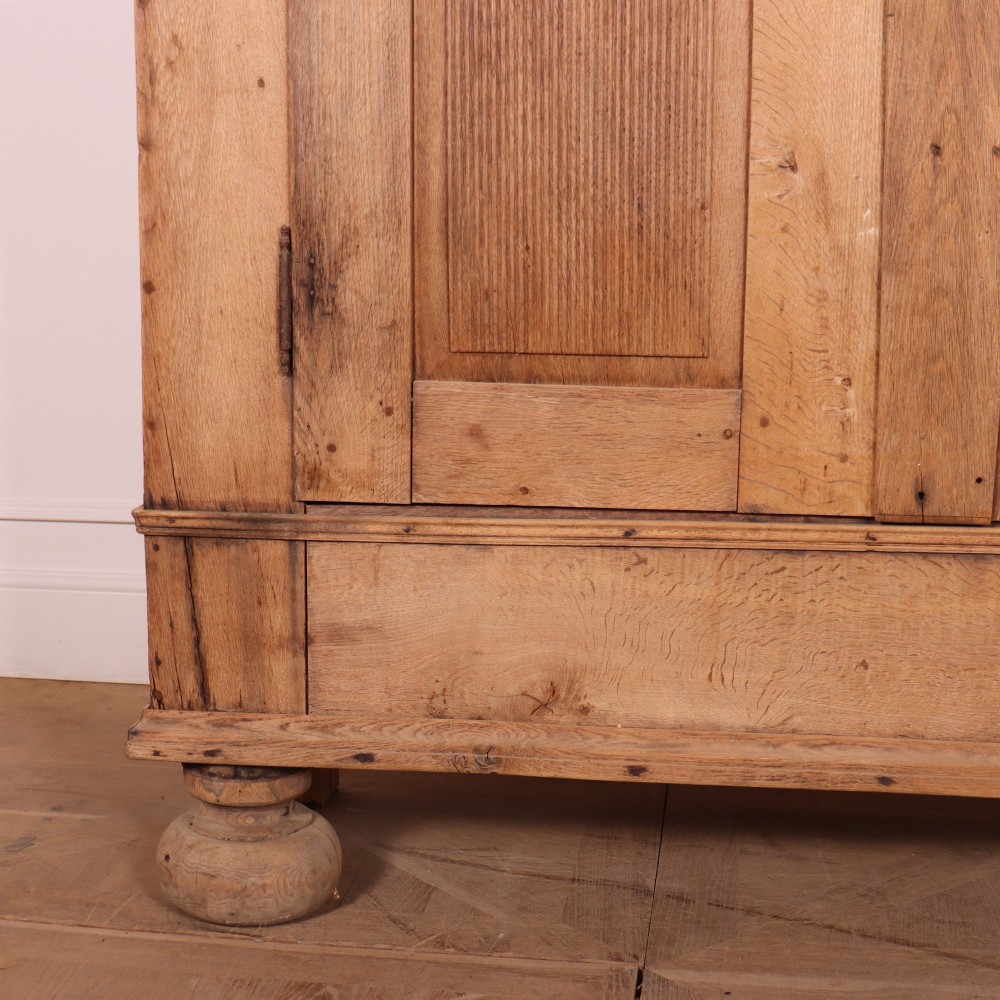 A freestanding antique Danish oak wardrobe featuring a flared top cornice, double doors with reeded panels, and heavy turned bun feet. View IV