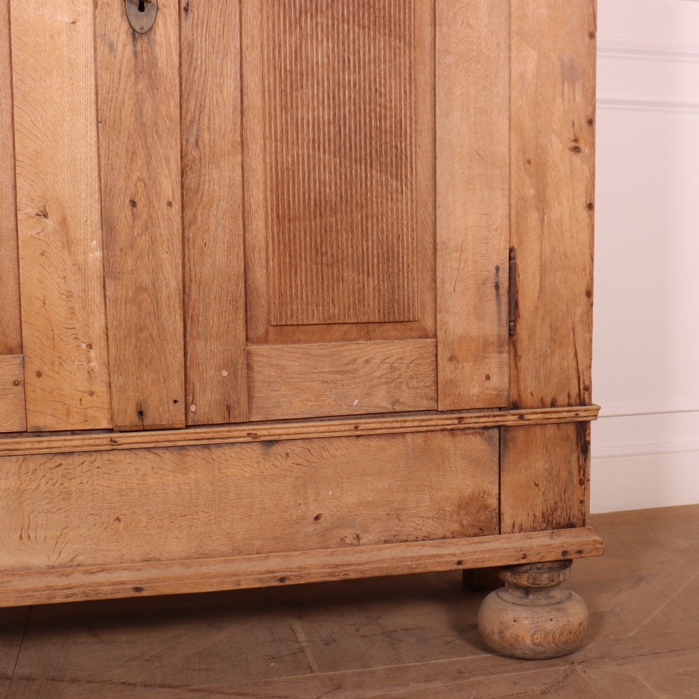 A freestanding antique Danish oak wardrobe featuring a flared top cornice, double doors with reeded panels, and heavy turned bun feet. View V