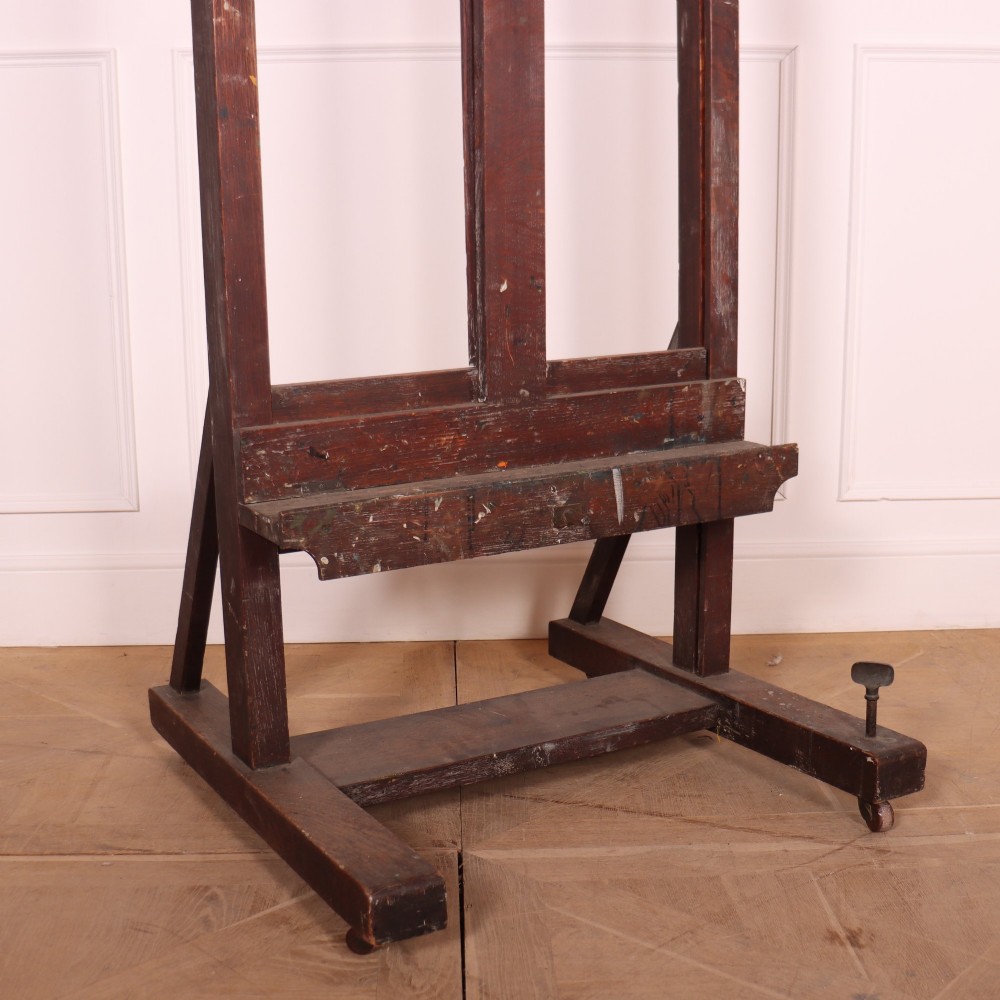 A floor-standing antique dark oak studio easel featuring an adjustable vertical central mast and a wide H-frame base with castors. View IV