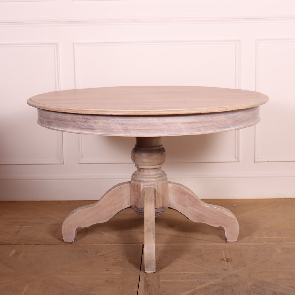 A circular bleached oak breakfast table with a thick turned central pedestal and four splayed legs.