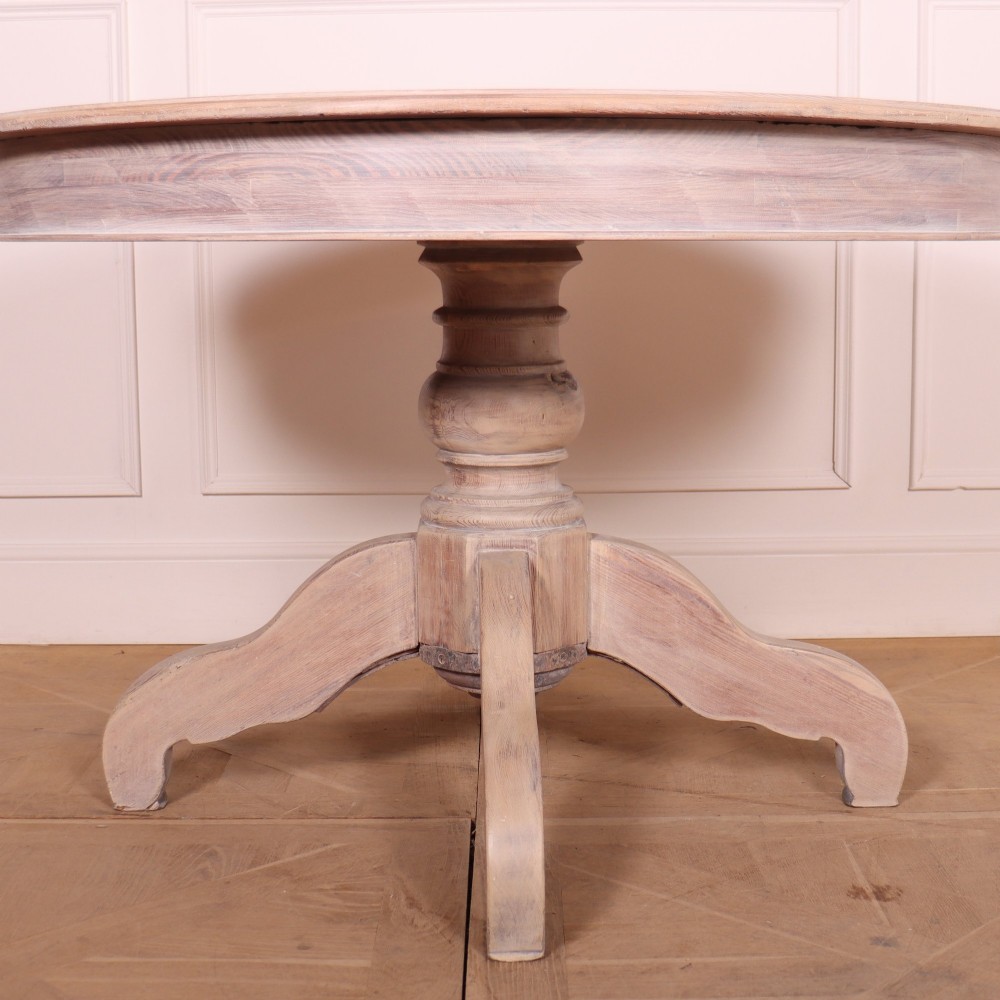 A circular bleached oak breakfast table with a thick turned central pedestal and four splayed legs. View II