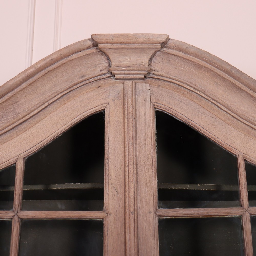 A large Dutch bleached oak display cabinet featuring an arched glazed top section with glass doors and a lower cupboard base supported on bun feet. View II