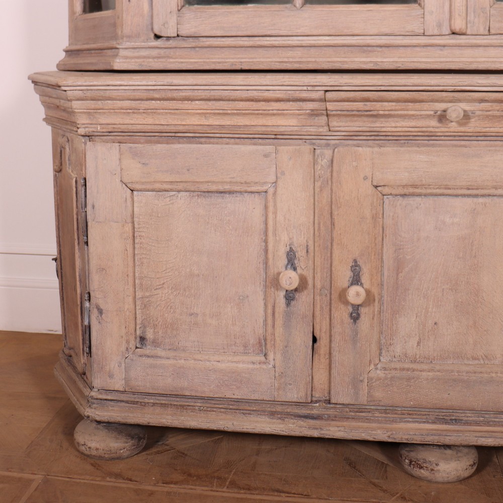 A large Dutch bleached oak display cabinet featuring an arched glazed top section with glass doors and a lower cupboard base supported on bun feet. View III