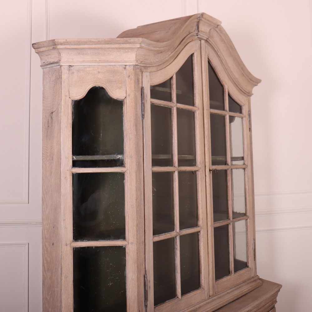 A large Dutch bleached oak display cabinet featuring an arched glazed top section with glass doors and a lower cupboard base supported on bun feet. View VII
