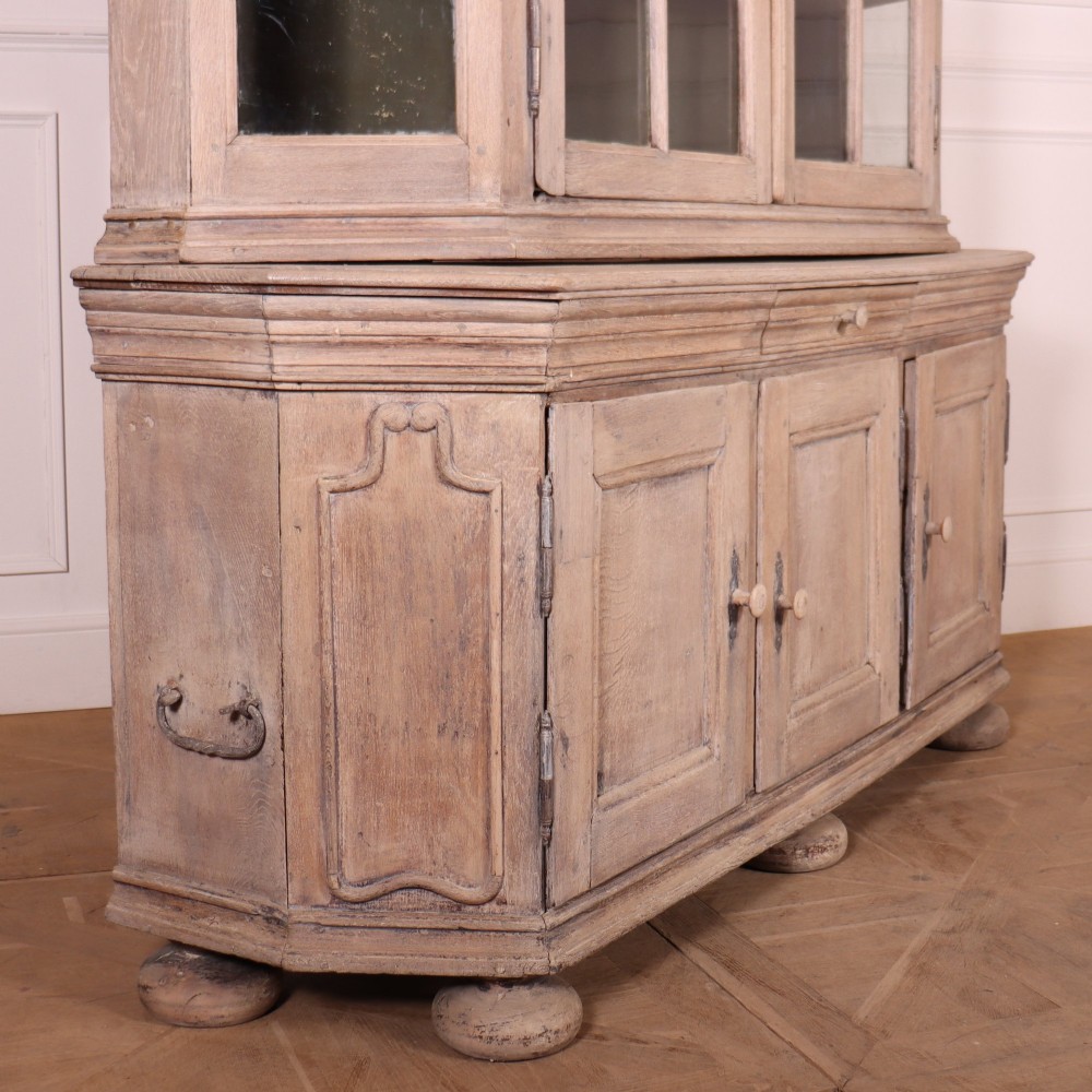 A large Dutch bleached oak display cabinet featuring an arched glazed top section with glass doors and a lower cupboard base supported on bun feet. View VIII