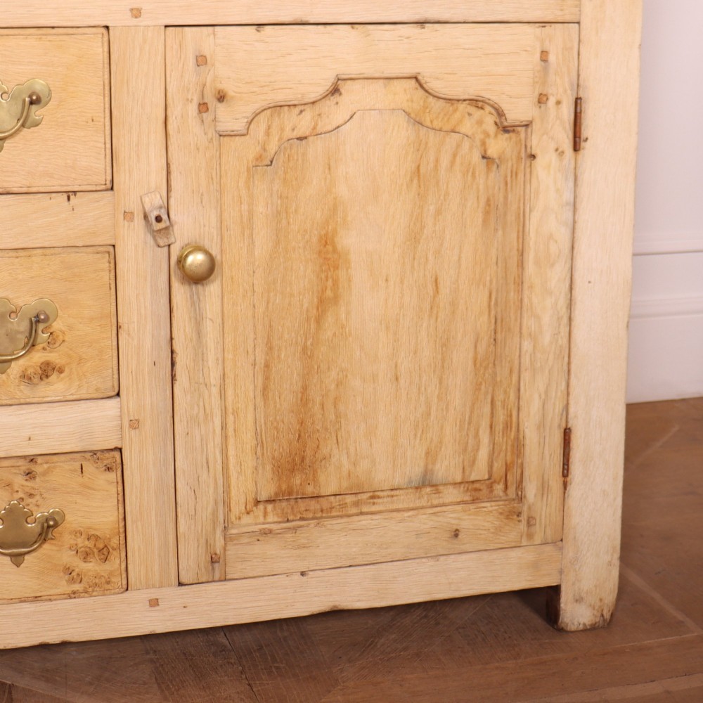 A wide bleached oak dresser base featuring six drawers with brass drop handles and two arched panelled cupboard doors. View VI