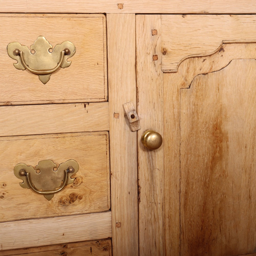A wide bleached oak dresser base featuring six drawers with brass drop handles and two arched panelled cupboard doors. View VII