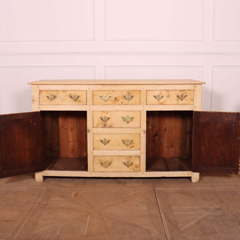 A wide bleached oak dresser base featuring six drawers with brass drop handles and two arched panelled cupboard doors. View VIII