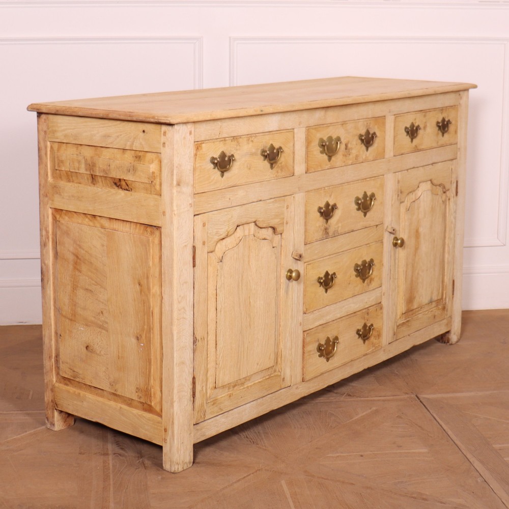 A wide bleached oak dresser base featuring six drawers with brass drop handles and two arched panelled cupboard doors. View IX