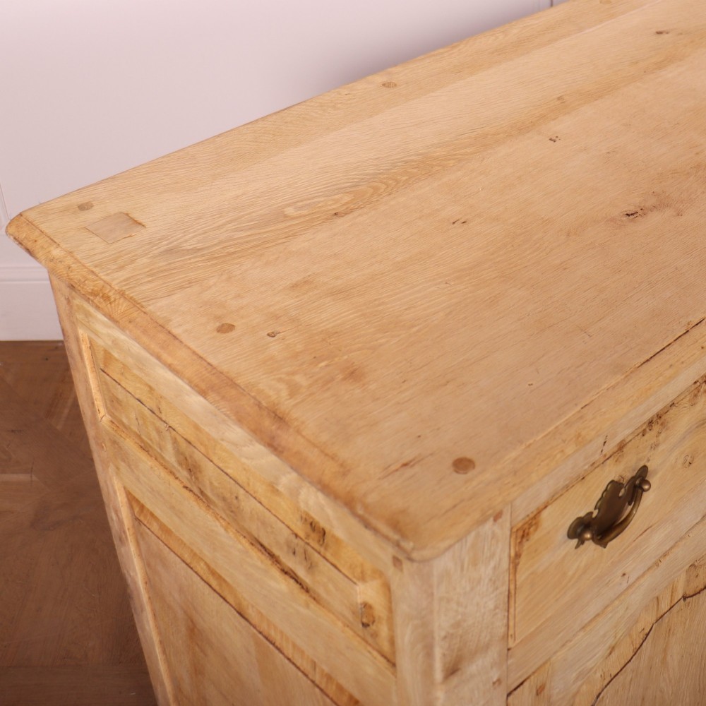 A wide bleached oak dresser base featuring six drawers with brass drop handles and two arched panelled cupboard doors. View X