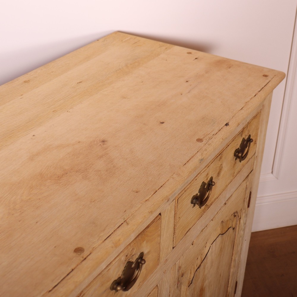 A wide bleached oak dresser base featuring six drawers with brass drop handles and two arched panelled cupboard doors. View XI