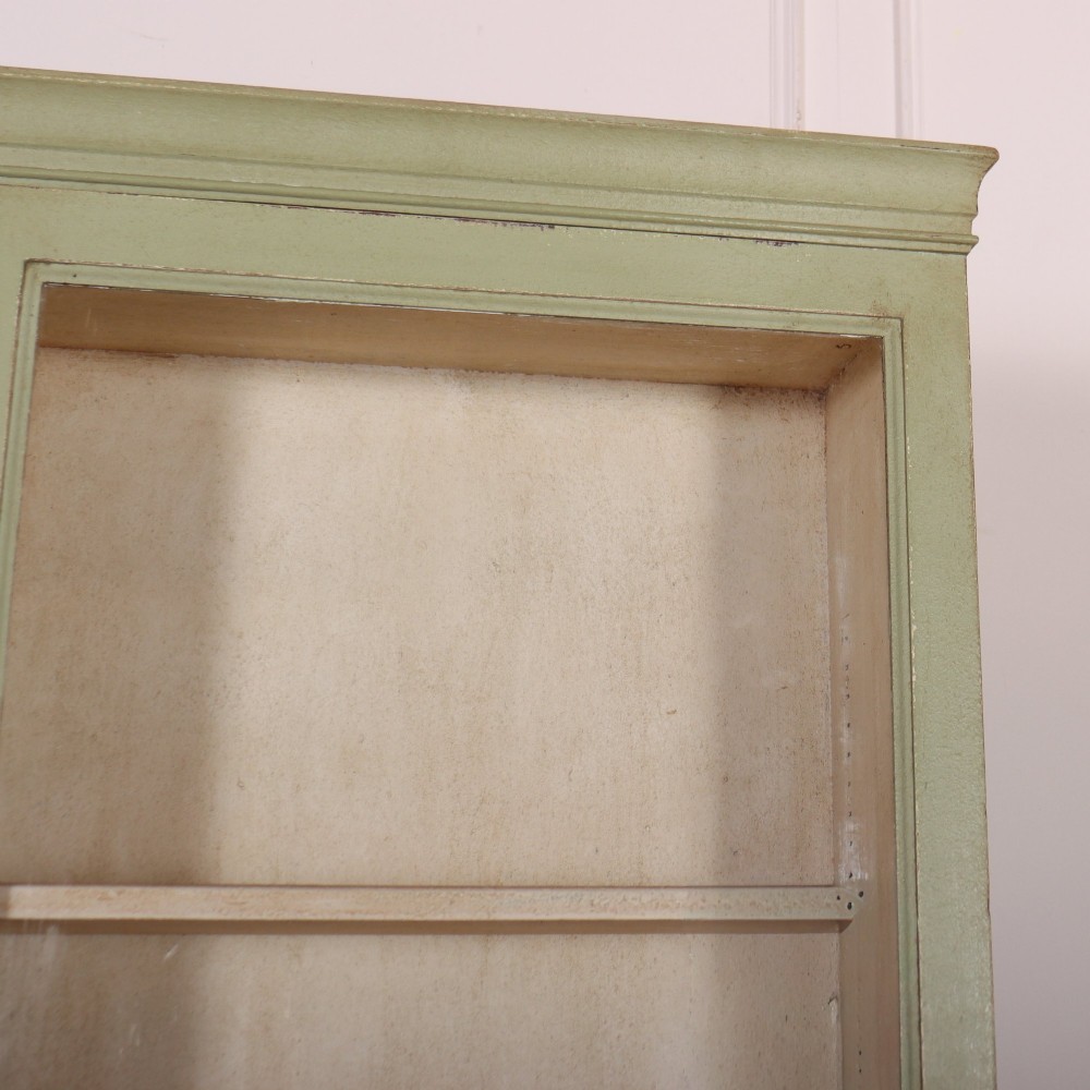 A tall sage green painted bookcase featuring two upper glazed doors revealing interior shelving, resting upon a base cabinet with two panelled doors. View III