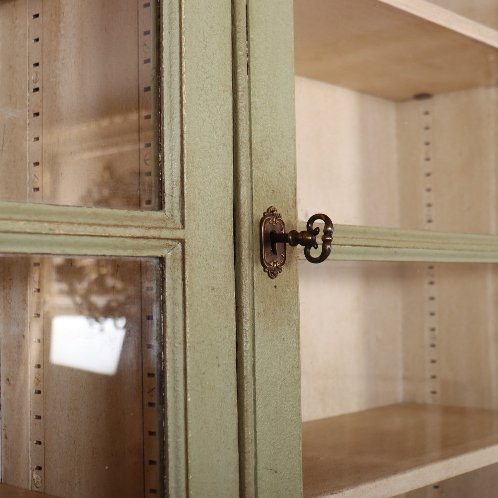 A tall sage green painted bookcase featuring two upper glazed doors revealing interior shelving, resting upon a base cabinet with two panelled doors. View V