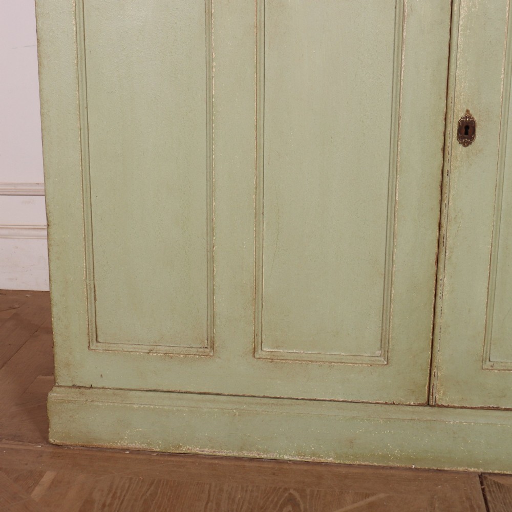 A tall sage green painted bookcase featuring two upper glazed doors revealing interior shelving, resting upon a base cabinet with two panelled doors. View VI