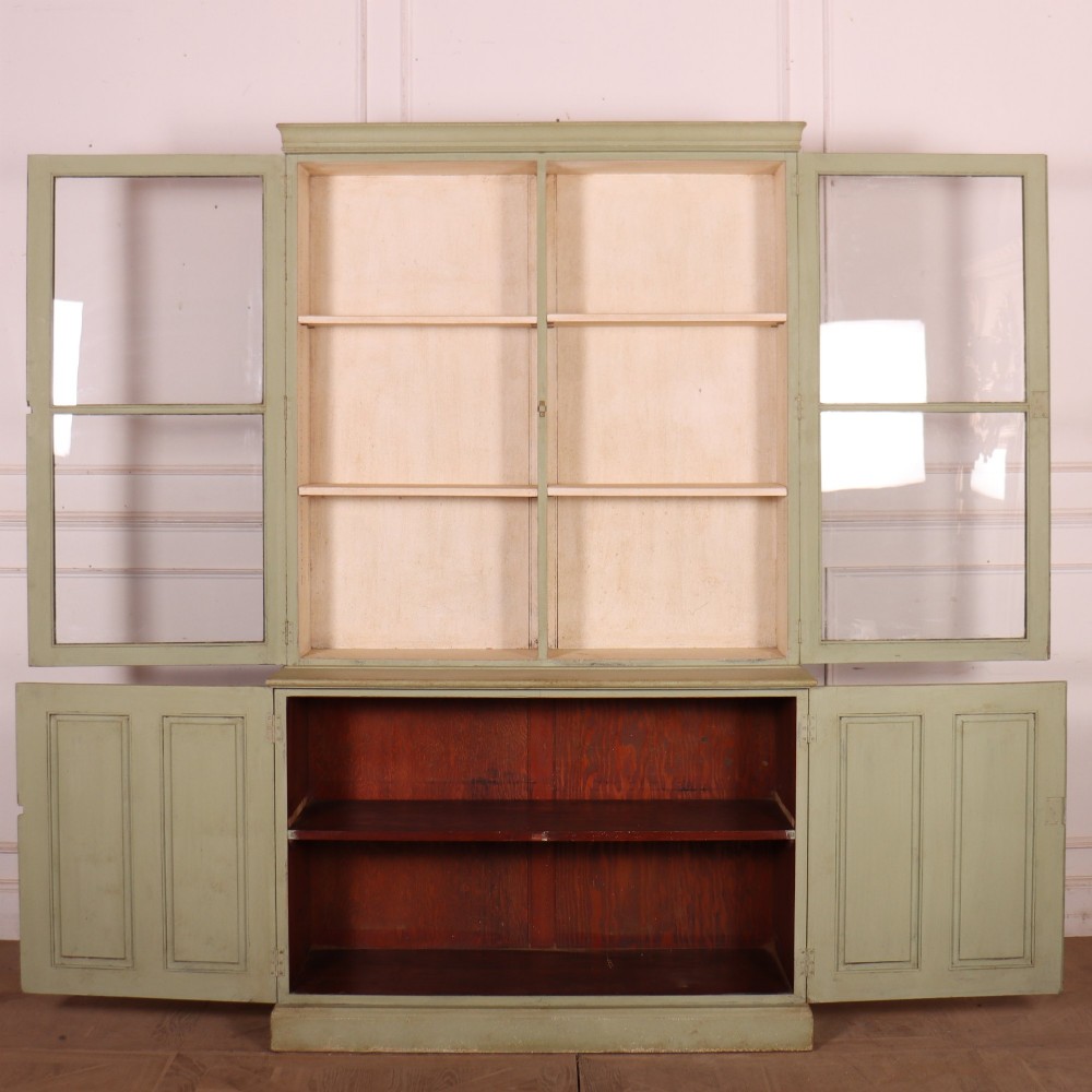 A tall sage green painted bookcase featuring two upper glazed doors revealing interior shelving, resting upon a base cabinet with two panelled doors. View VIII