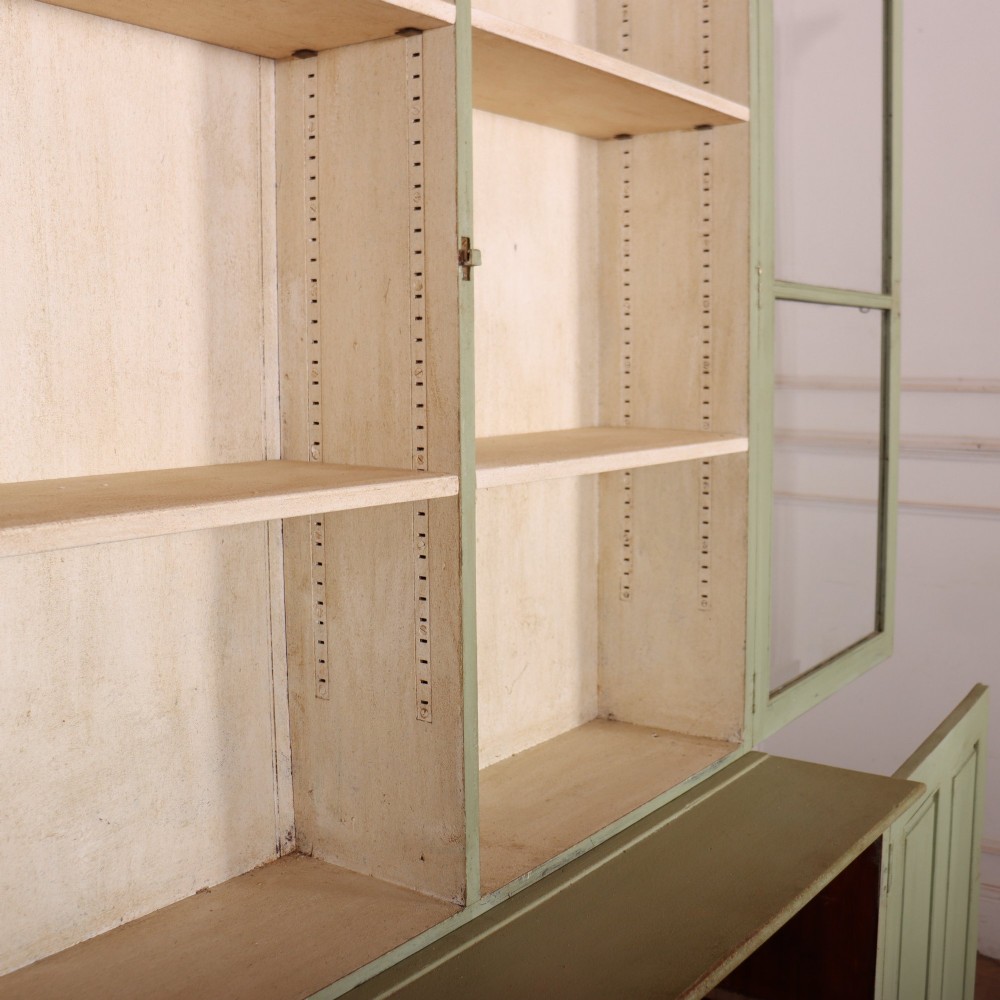 A tall sage green painted bookcase featuring two upper glazed doors revealing interior shelving, resting upon a base cabinet with two panelled doors. View IX