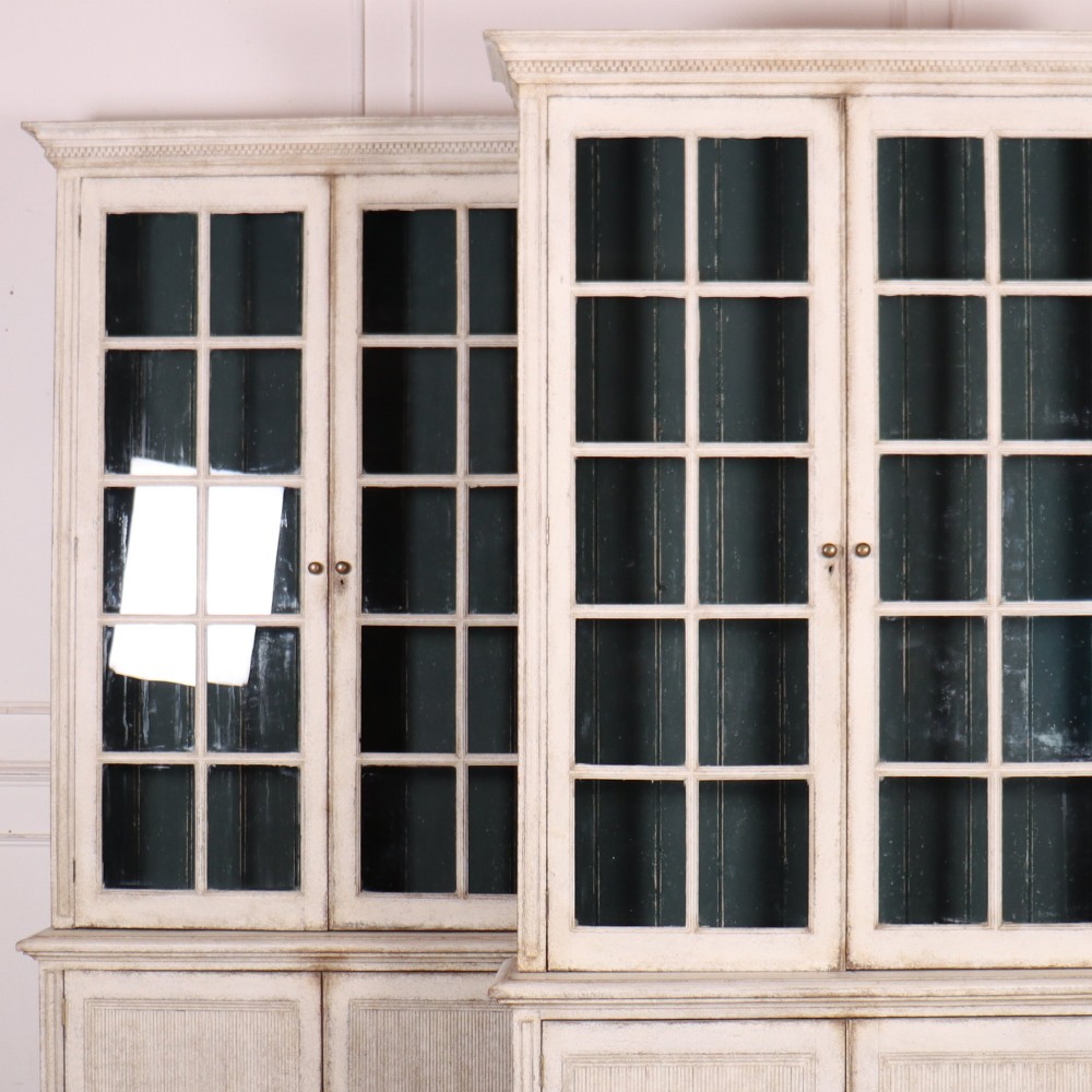 A pair of tall Swedish Gustavian style off-white painted bookcases featuring glazed upper doors with dark green interior backs above lower cupboards. View II