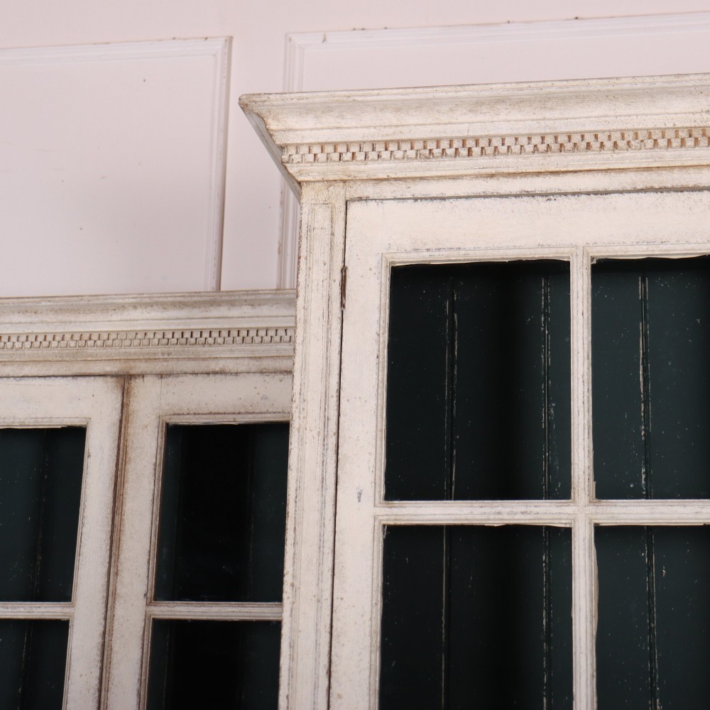 A pair of tall Swedish Gustavian style off-white painted bookcases featuring glazed upper doors with dark green interior backs above lower cupboards. View III