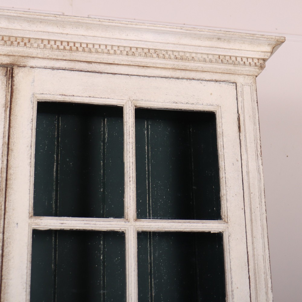 A pair of tall Swedish Gustavian style off-white painted bookcases featuring glazed upper doors with dark green interior backs above lower cupboards. View IV
