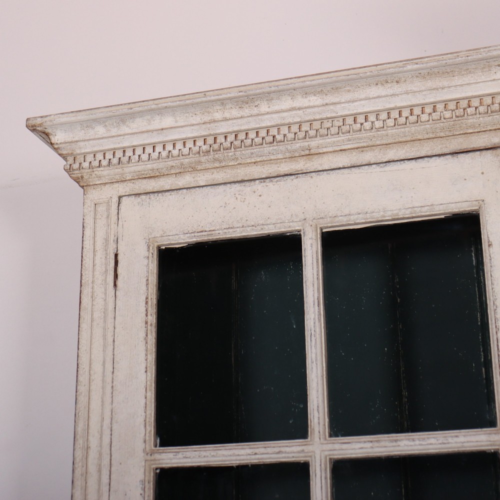A pair of tall Swedish Gustavian style off-white painted bookcases featuring glazed upper doors with dark green interior backs above lower cupboards. View V
