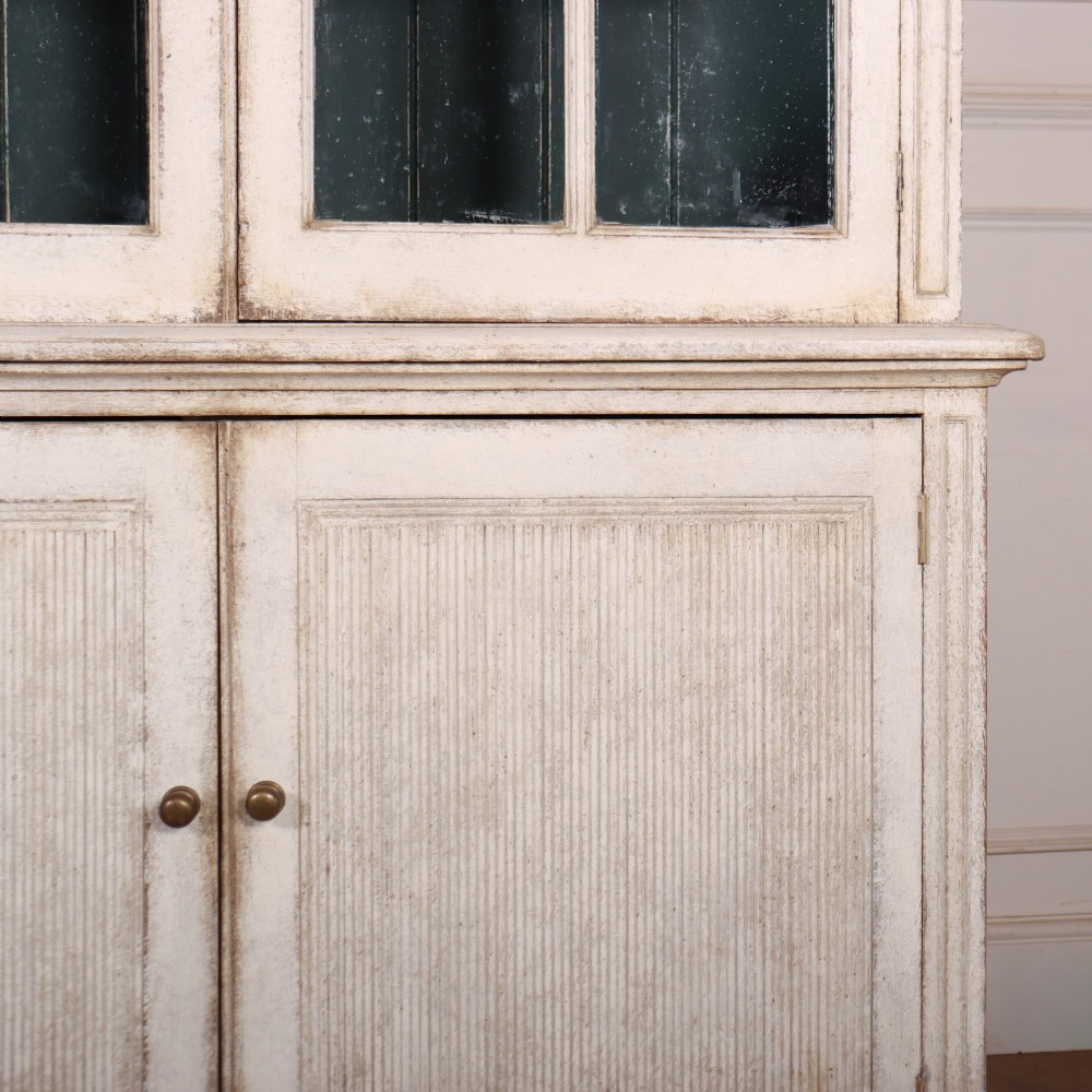 A pair of tall Swedish Gustavian style off-white painted bookcases featuring glazed upper doors with dark green interior backs above lower cupboards. View VII