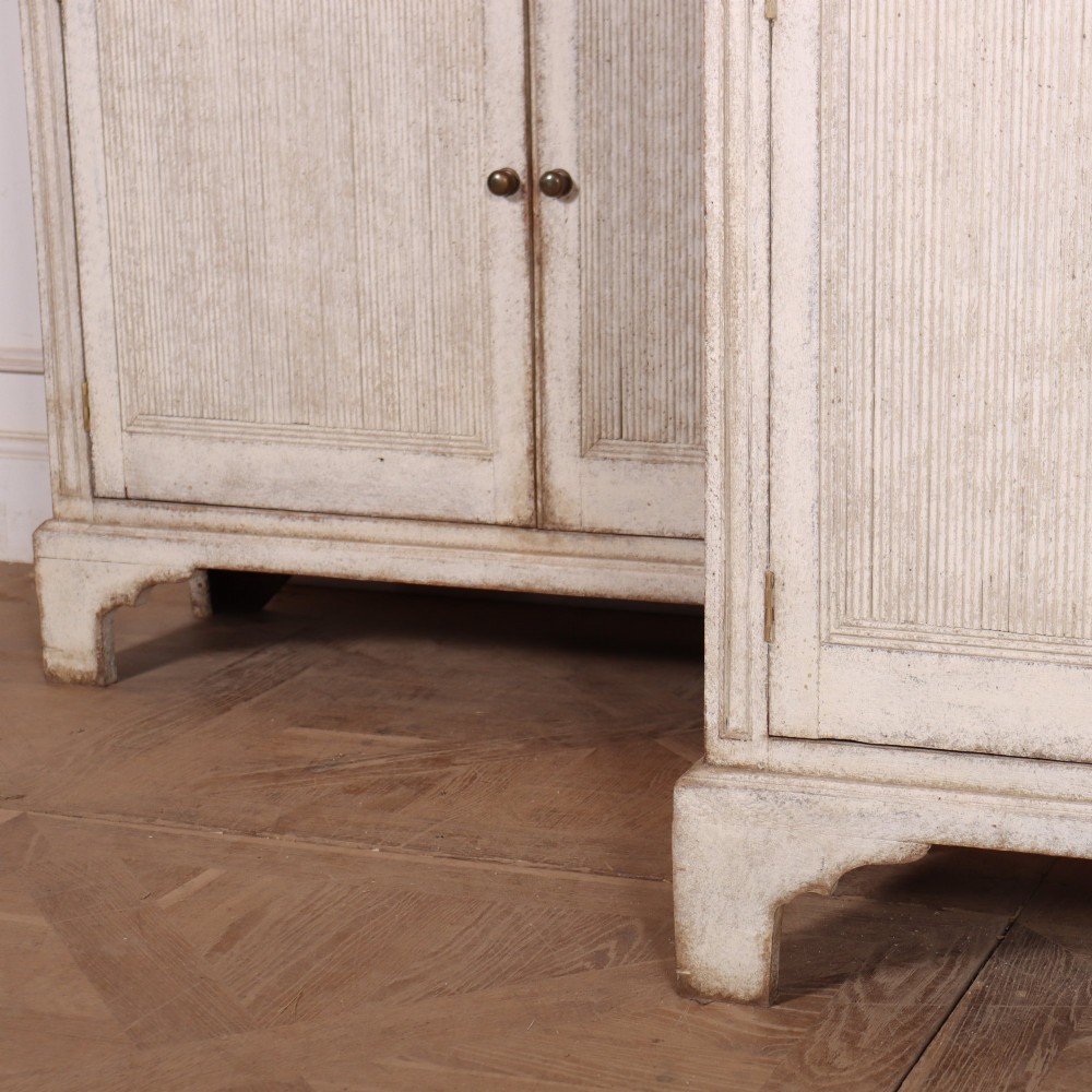 A pair of tall Swedish Gustavian style off-white painted bookcases featuring glazed upper doors with dark green interior backs above lower cupboards. View IX