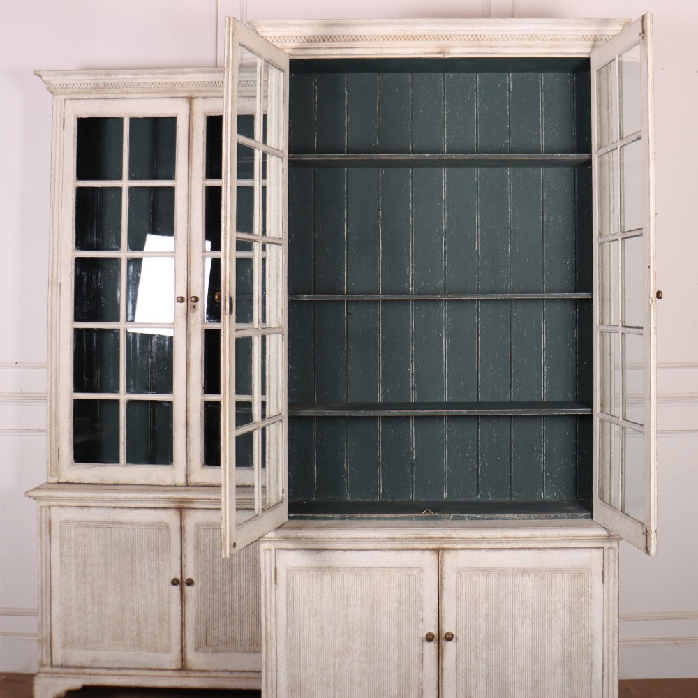 A pair of tall Swedish Gustavian style off-white painted bookcases featuring glazed upper doors with dark green interior backs above lower cupboards. View XI
