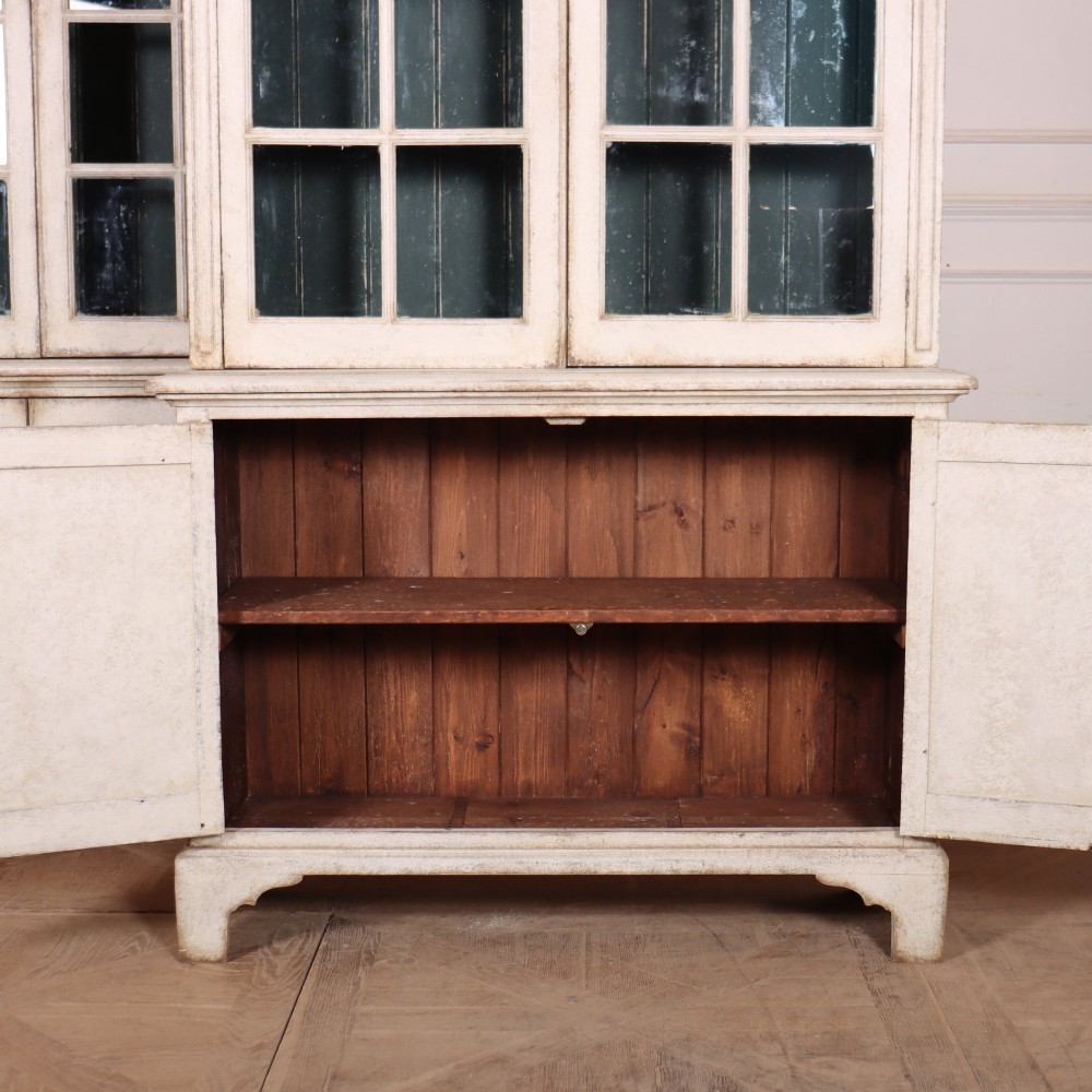 A pair of tall Swedish Gustavian style off-white painted bookcases featuring glazed upper doors with dark green interior backs above lower cupboards. View XIII