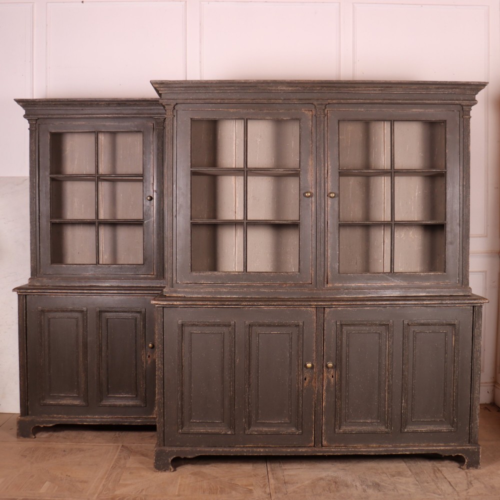 A pair of dark grey painted wooden dressers featuring glazed upper display cabinets with square mullions above panelled two-door lower cupboards.