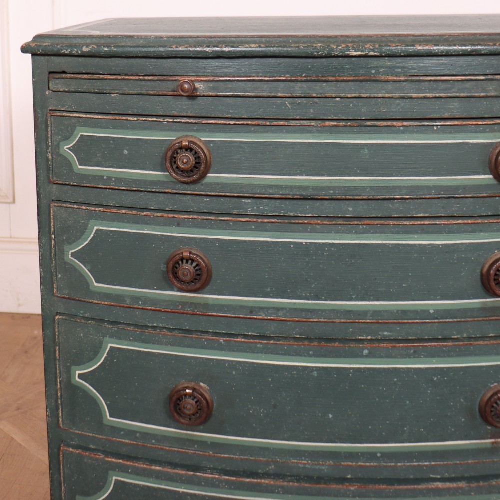 A deep green painted bowfront bedside chest of drawers featuring light green decorative panel outline details, brass ring handles, and splayed legs. View II