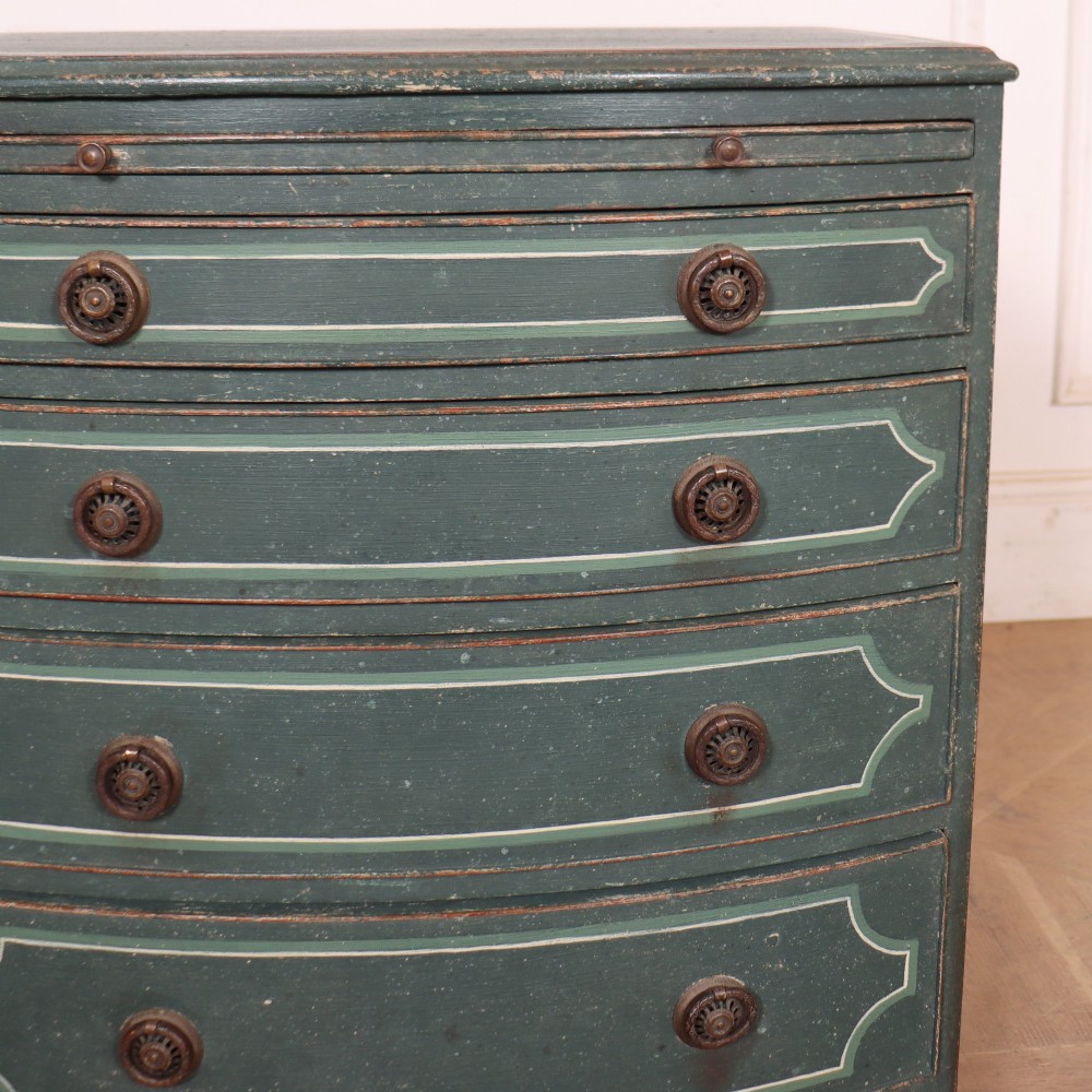 A deep green painted bowfront bedside chest of drawers featuring light green decorative panel outline details, brass ring handles, and splayed legs. View III