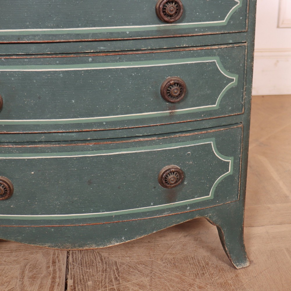 A deep green painted bowfront bedside chest of drawers featuring light green decorative panel outline details, brass ring handles, and splayed legs. View IV