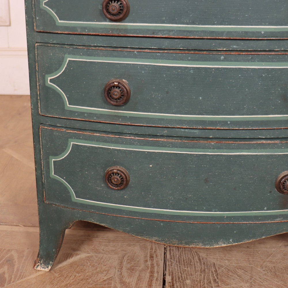 A deep green painted bowfront bedside chest of drawers featuring light green decorative panel outline details, brass ring handles, and splayed legs. View V