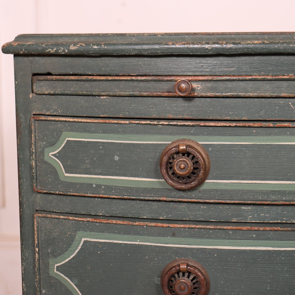 A deep green painted bowfront bedside chest of drawers featuring light green decorative panel outline details, brass ring handles, and splayed legs. View VI