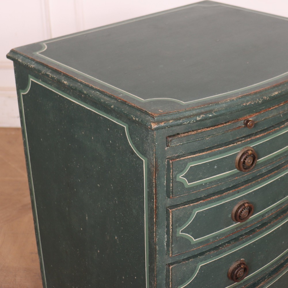 A deep green painted bowfront bedside chest of drawers featuring light green decorative panel outline details, brass ring handles, and splayed legs. View VIII