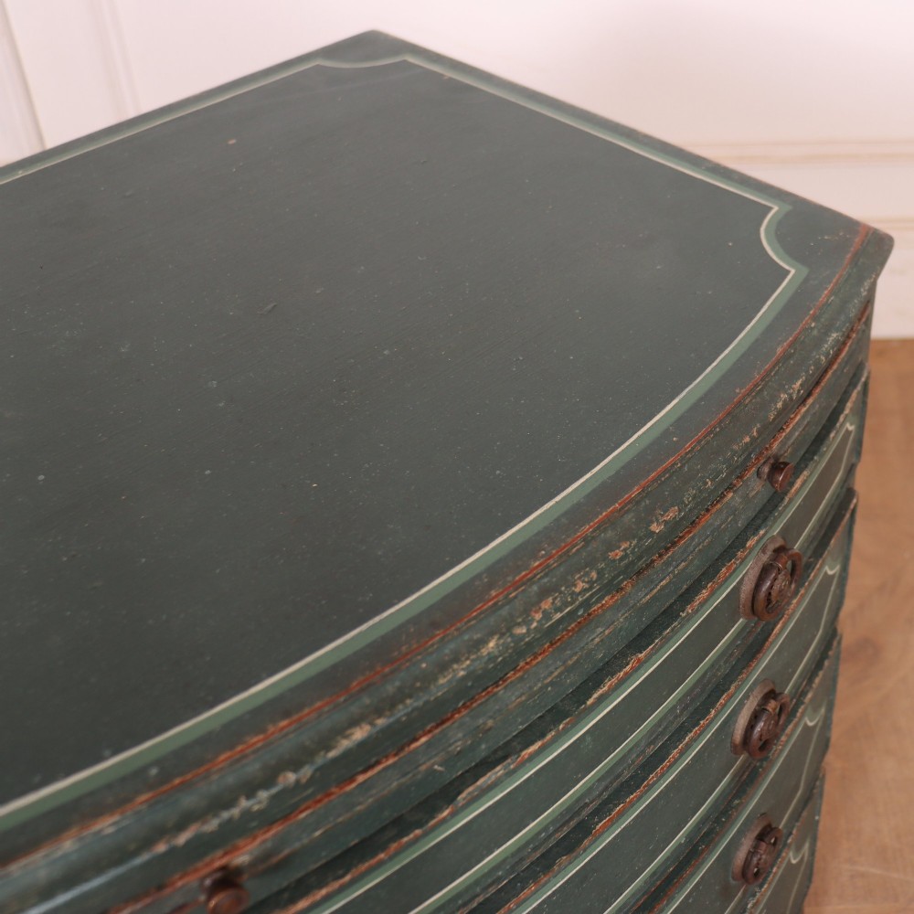 A deep green painted bowfront bedside chest of drawers featuring light green decorative panel outline details, brass ring handles, and splayed legs. View IX