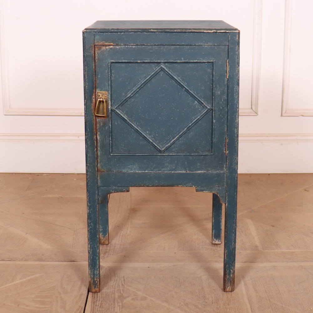 A small Swedish blue painted wood bedside cabinet with a carved diamond panel on the single door and a brass pull handle.
