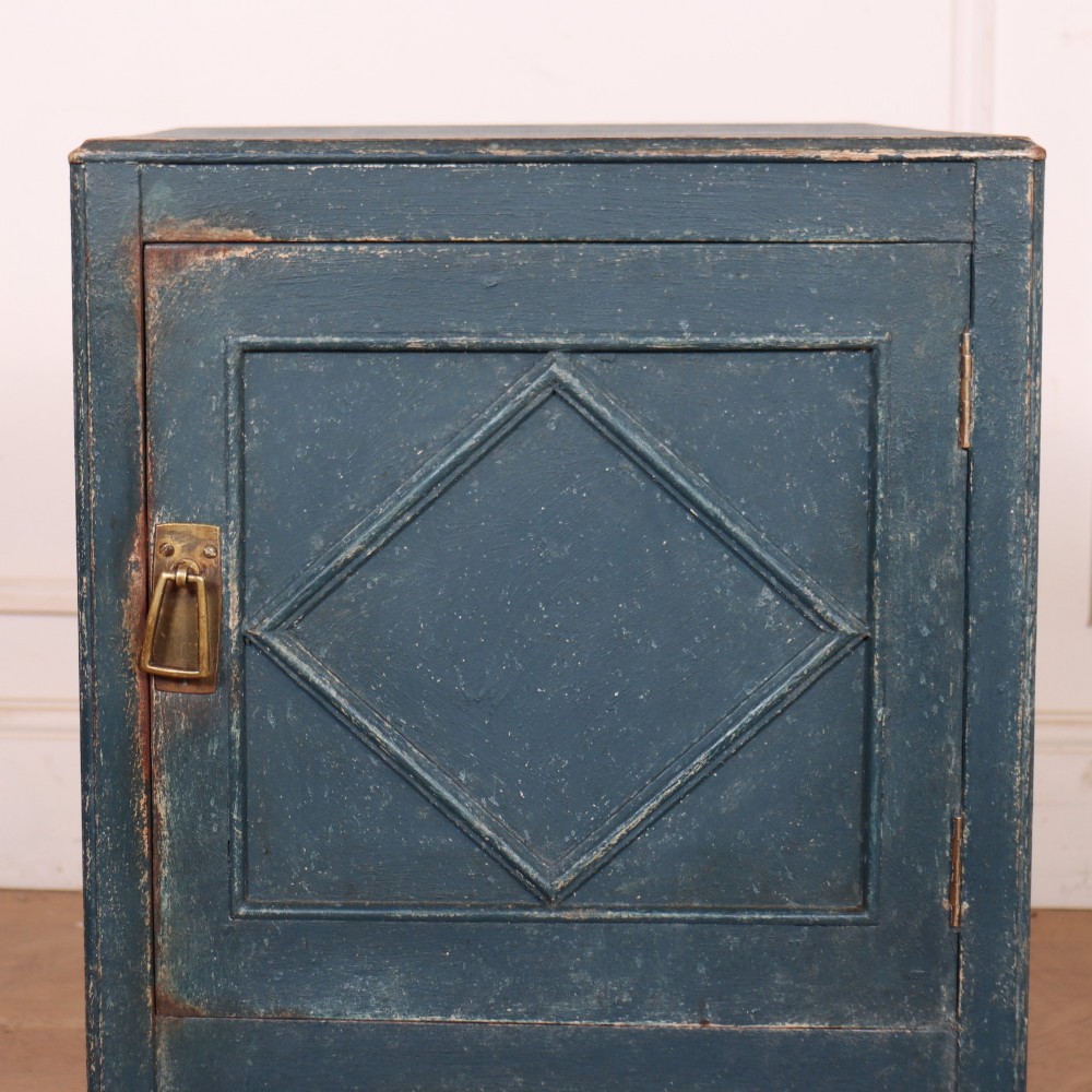 A small Swedish blue painted wood bedside cabinet with a carved diamond panel on the single door and a brass pull handle. View II