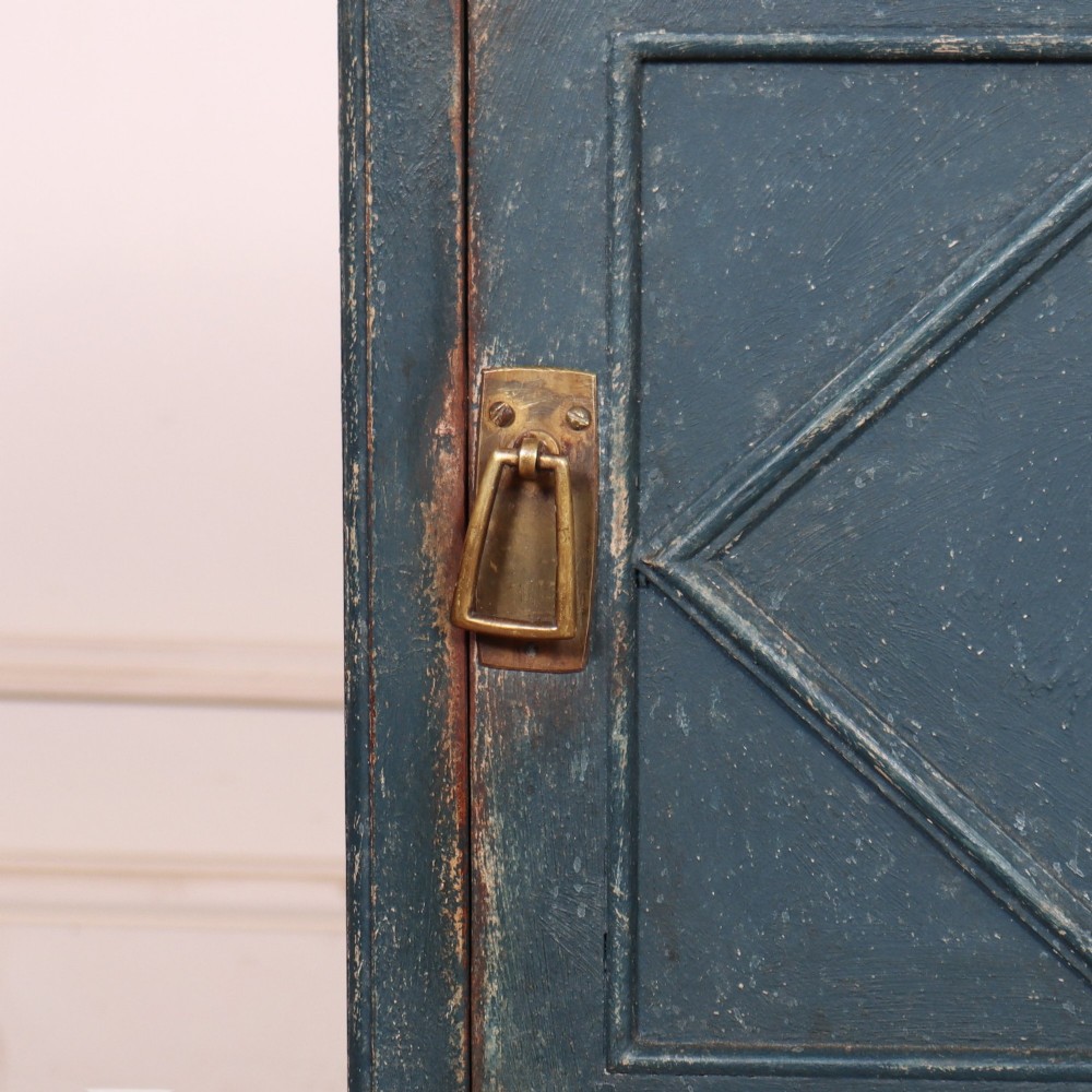 A small Swedish blue painted wood bedside cabinet with a carved diamond panel on the single door and a brass pull handle. View IV