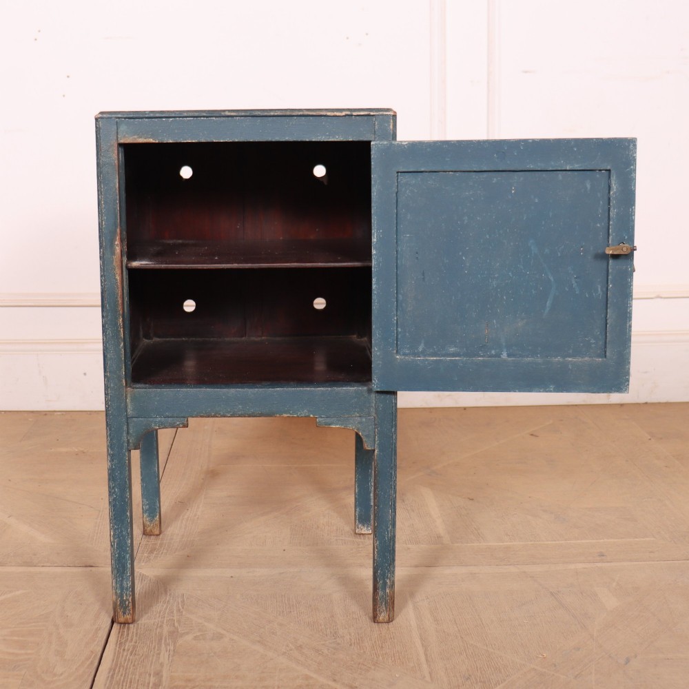 A small Swedish blue painted wood bedside cabinet with a carved diamond panel on the single door and a brass pull handle. View V