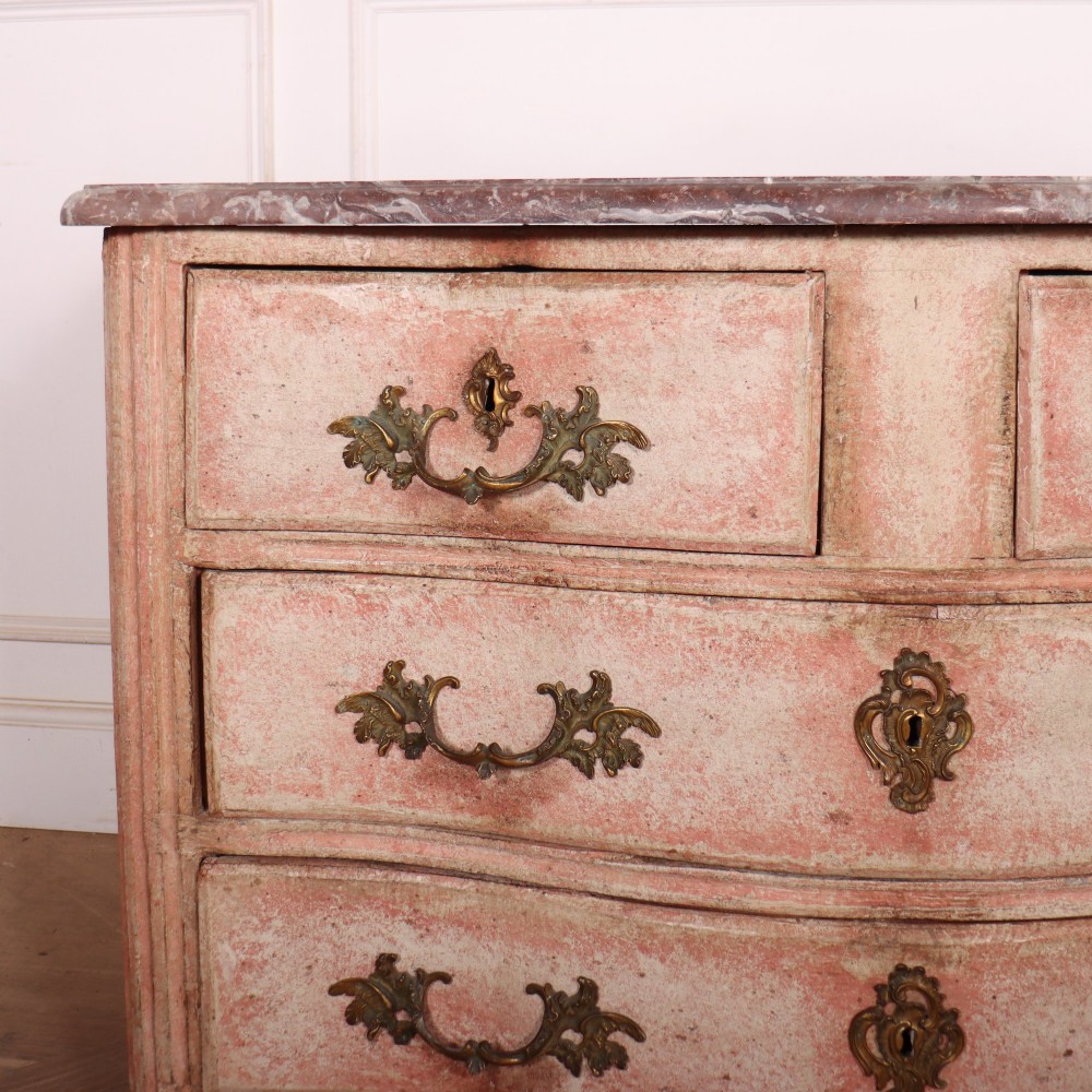 A Louis XV style French painted commode featuring a serpentine front, grey marble top, four drawers with rococo brass handles, and a distressed pale pink painted finish. View II