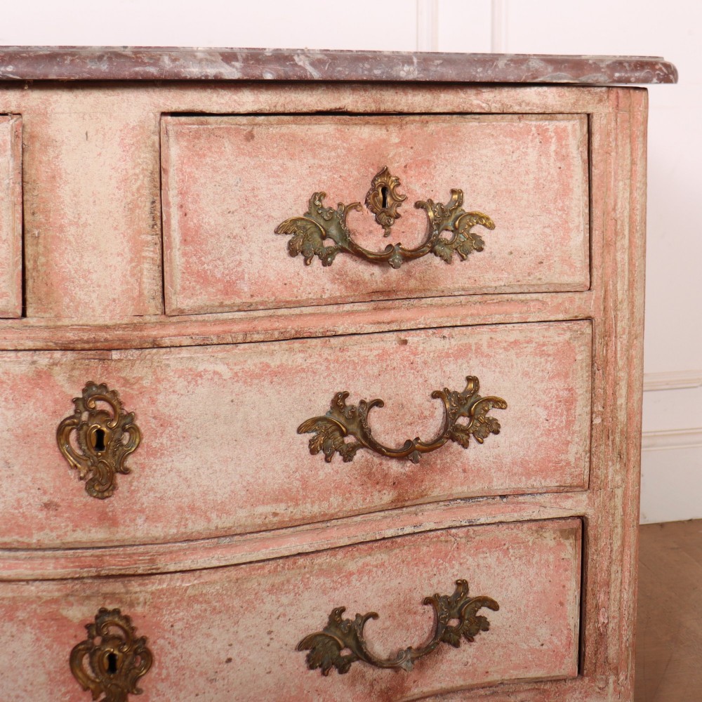 A Louis XV style French painted commode featuring a serpentine front, grey marble top, four drawers with rococo brass handles, and a distressed pale pink painted finish. View IV