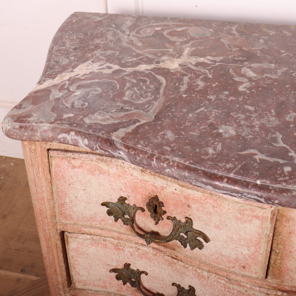A Louis XV style French painted commode featuring a serpentine front, grey marble top, four drawers with rococo brass handles, and a distressed pale pink painted finish. View VII