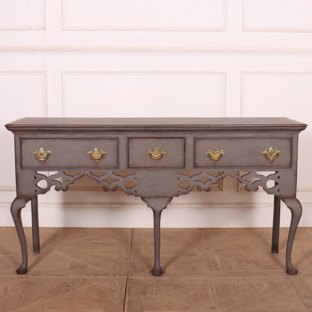 A grey-painted antique dresser base featuring three drawers with brass handles, a decorative pierced fretwork apron, and cabriole legs.